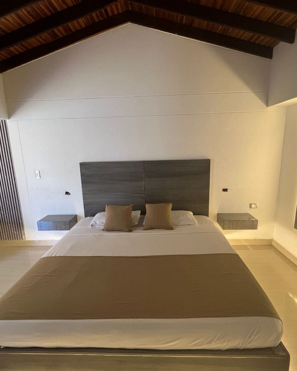 Suite Premium: la cama de frente, con cabecera de madera, mesas de noche flotantes y techo de vigas