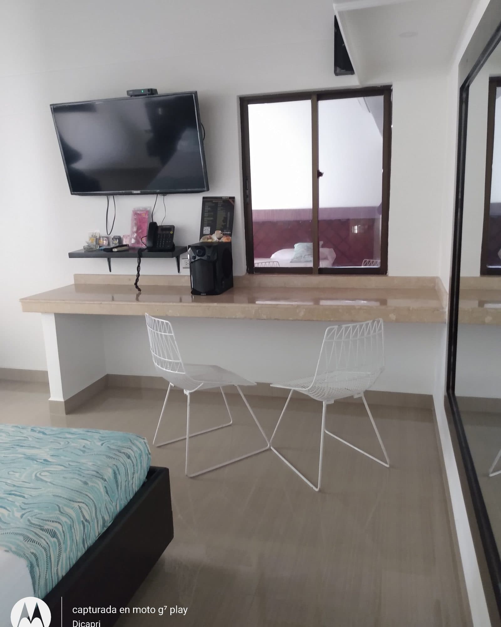 Suite Silver: mesa de mármol claro con dos sillas blancas de alambre y televisor, frente a la cama con cubrecama turquesa