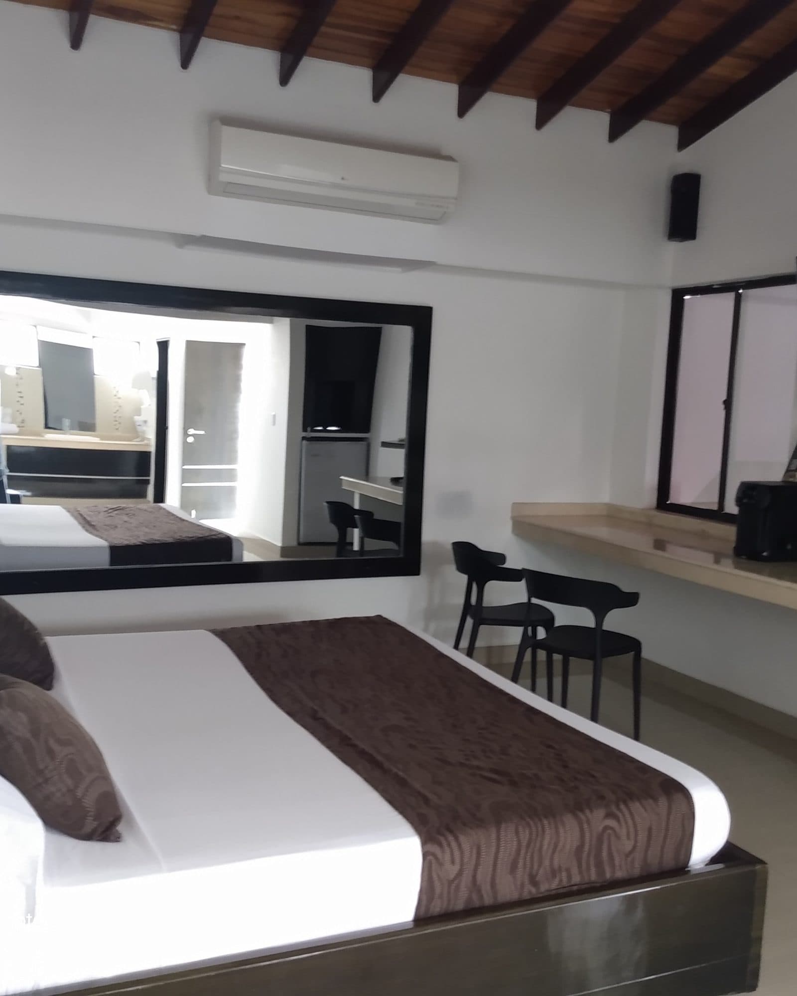 Suite Silver: espejo grande de pared que refleja la cama, con dos sillas negras en la mesa de mármol